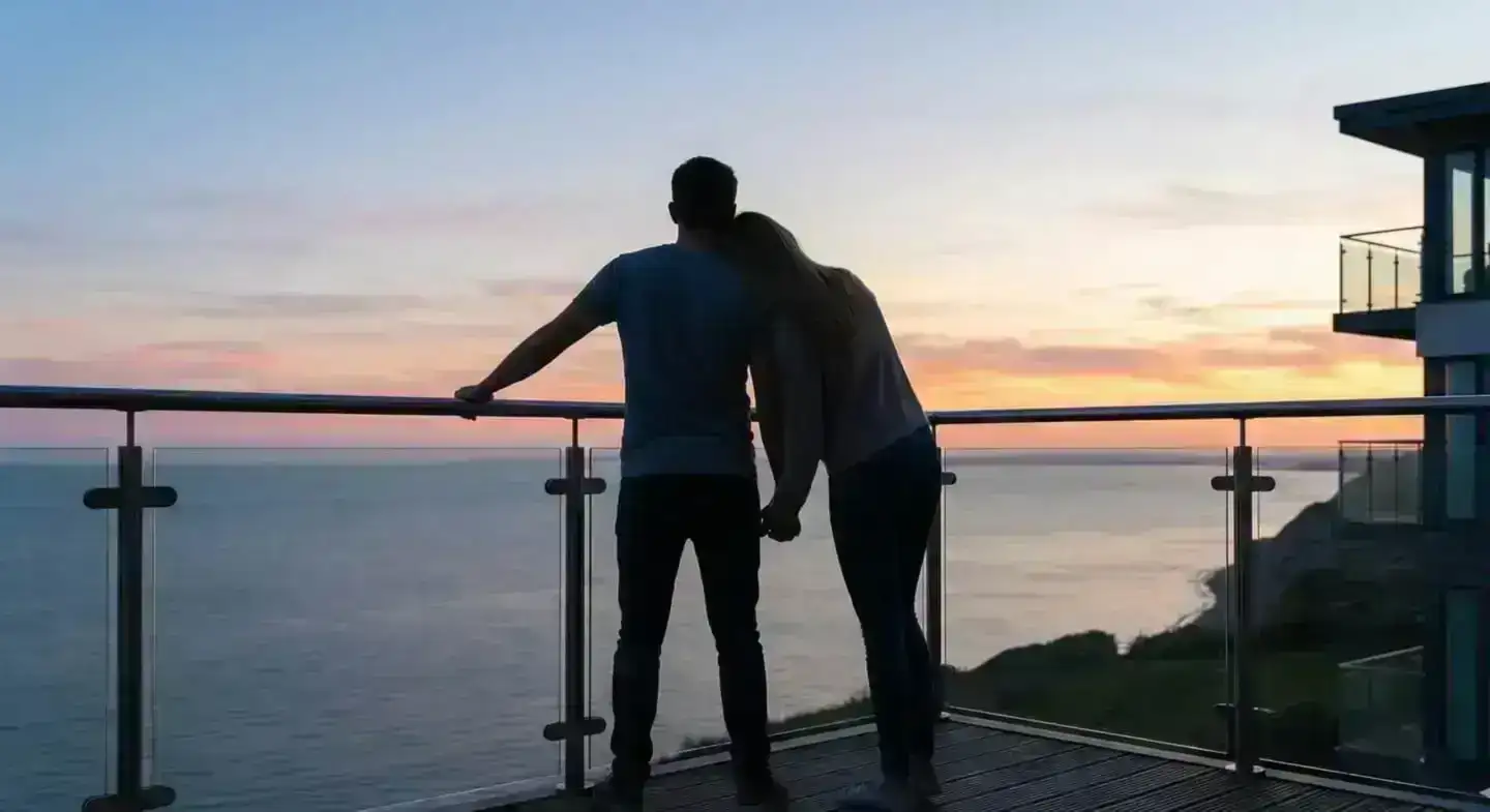 Couple enjoying the view from their holiday cottage balcony at sunset